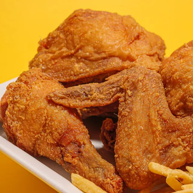 Delicious crispy fried chicken alongside golden French fries on a vibrant yellow backdrop.