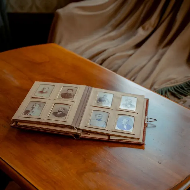 A vintage photo album lies open on a classic wooden table with a cozy fabric curtain backdrop.