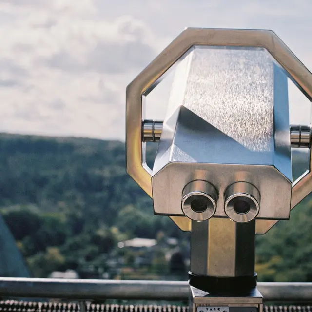 Stainless steel telescope pointing towards a lush, scenic landscape under a bright summer sky.