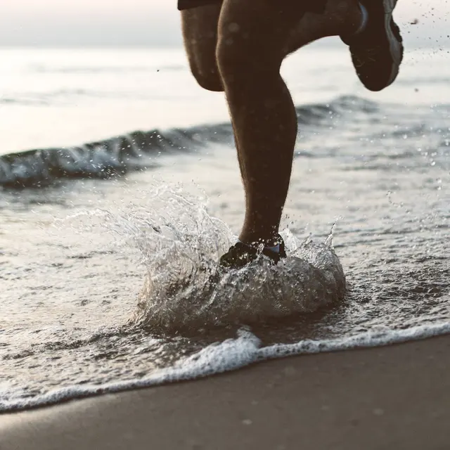 Dynamic shot of legs running on Palanga beach during sunrise, splashing water.