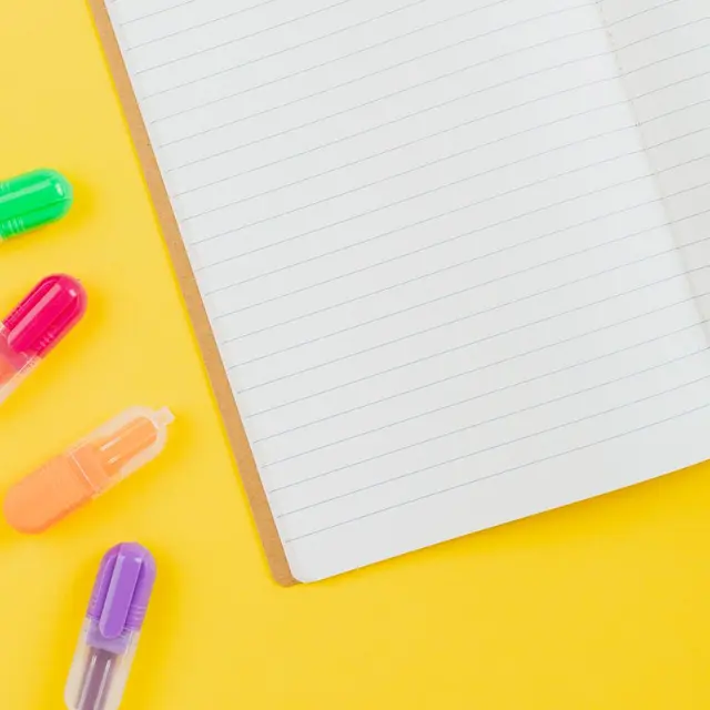 Flat lay of colorful highlighters and an open notebook on a vibrant yellow background.